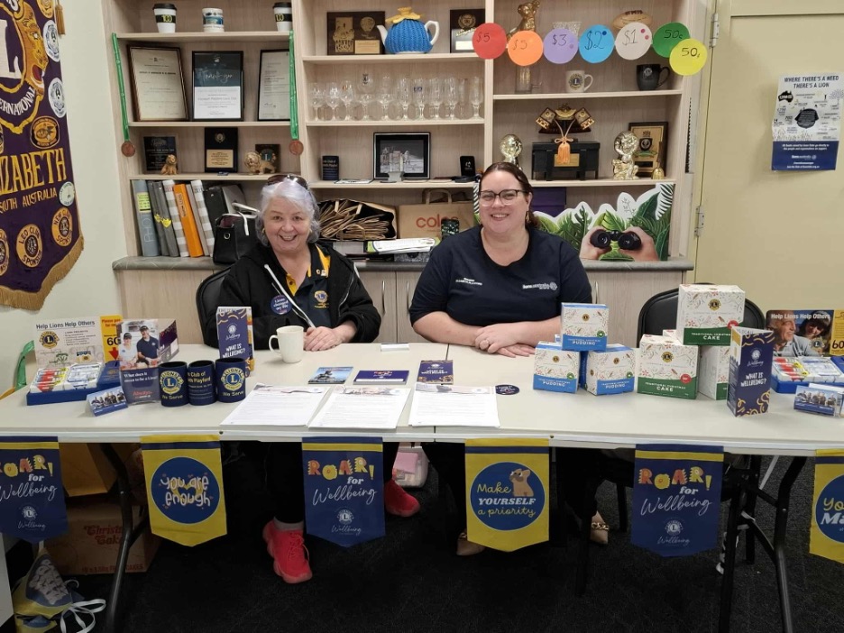 Two women smiling at a table providing mental health and wellness resources.