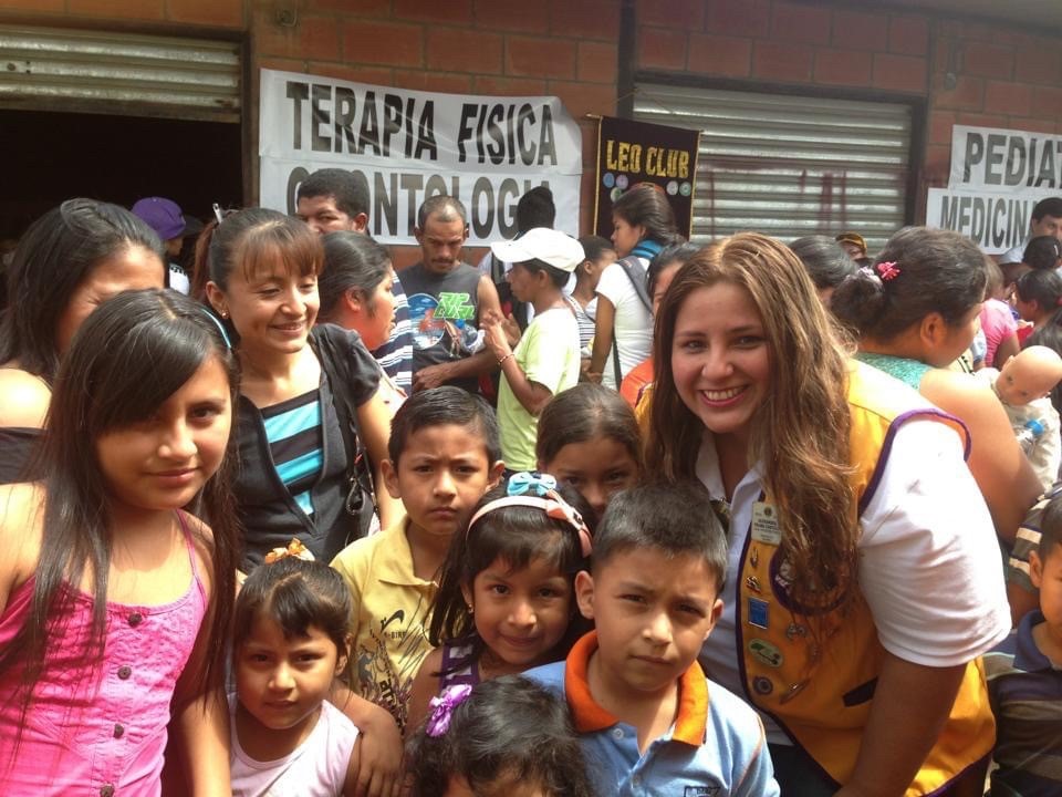 A Companheira Leão Alexandra sorri com um grande grupo de crianças durante um projeto de serviço comunitário.