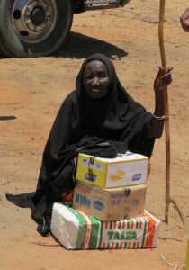 An elderly woman sits on the ground with food donated to her by Lions